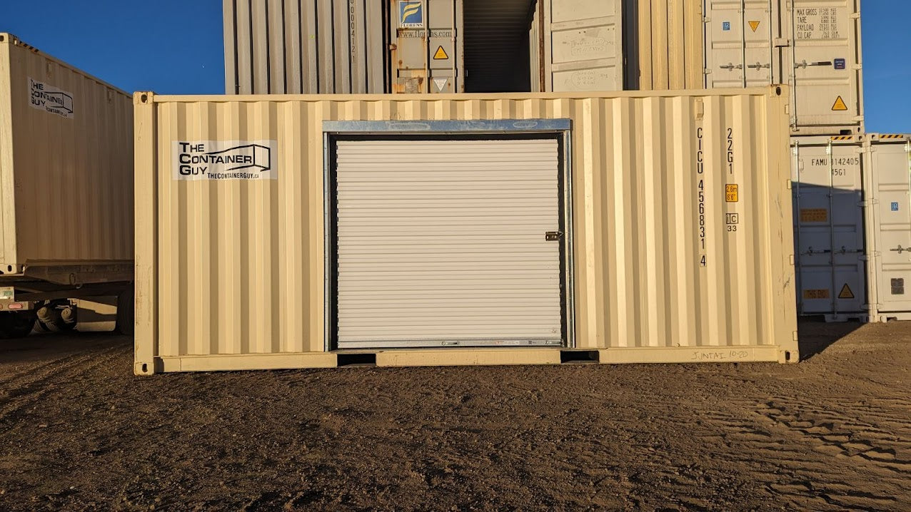 Beige shipping container with installed white roll-up door on the sidewall using a galvanized steel framing kit. Container sits on a dirt lot with other stacked containers in the background. Branding for “The Container Guy” is visible.