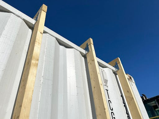 Galvanized steel brackets supporting vertical wood framing on white shipping container exterior
