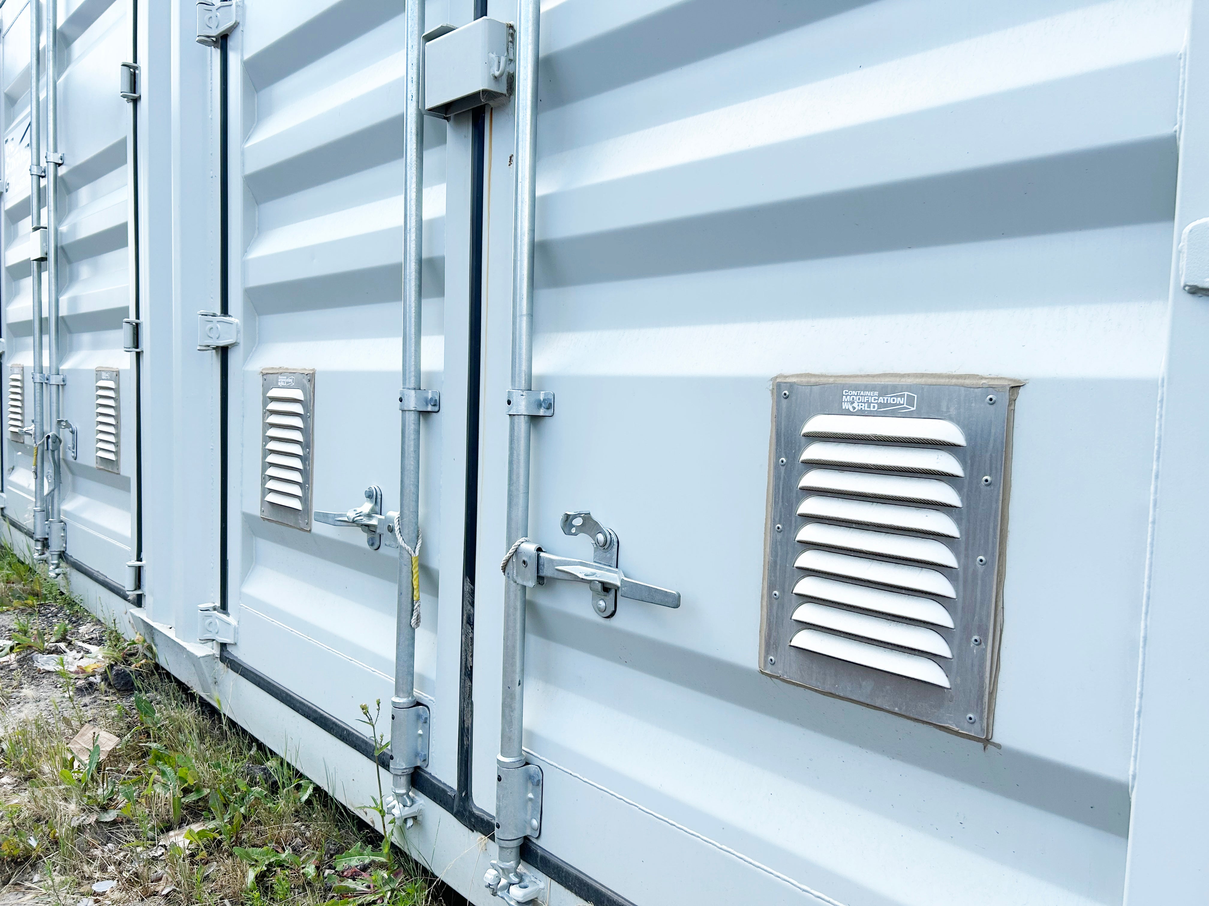 Close-up view of multiple white shipping container doors with Big Air 45 Louvered Gable Vents installed near the bottom for improved airflow and moisture control.