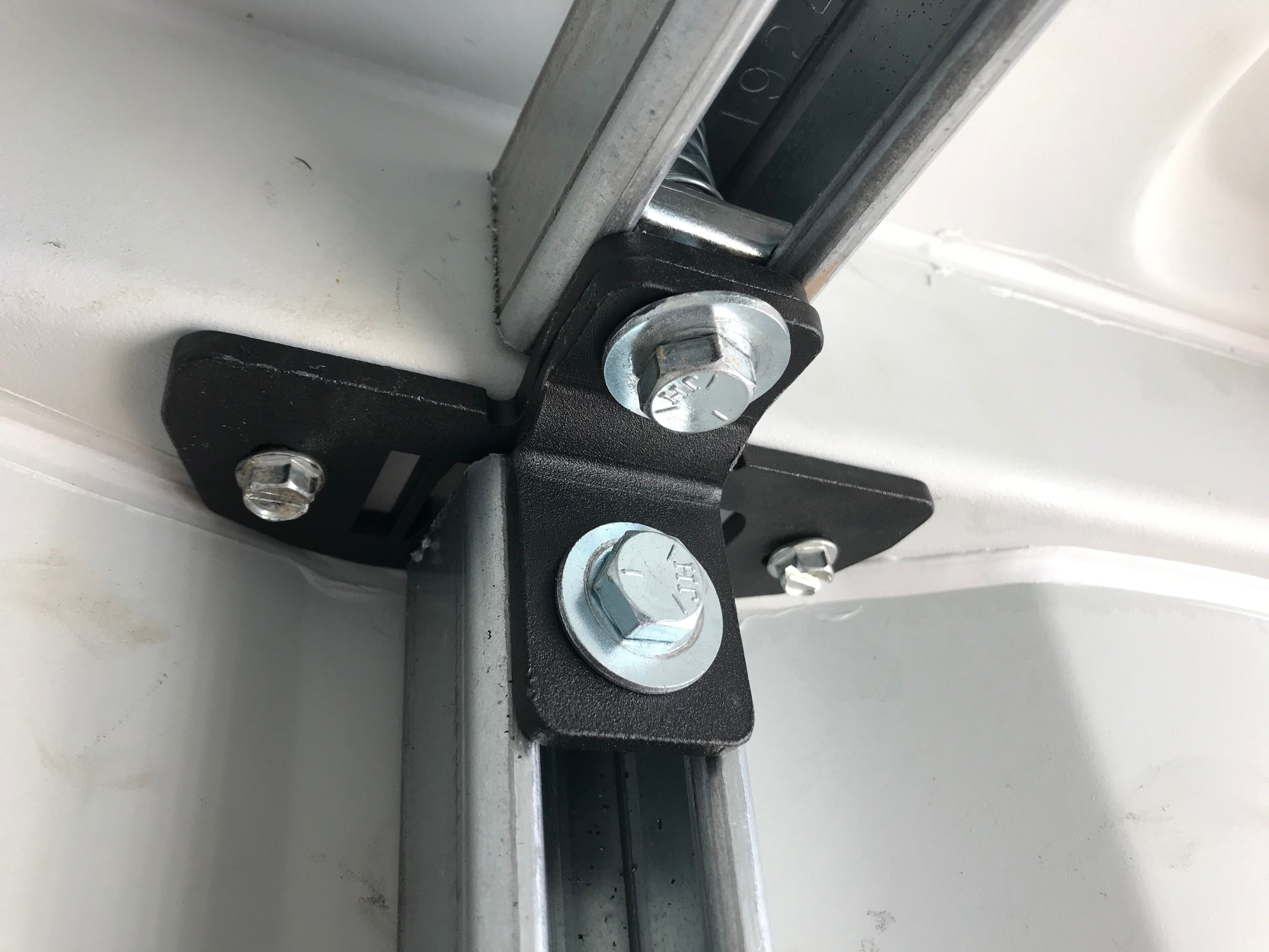 Close-up of black Container Strut Mount (CSM) bracket securing vertical and horizontal strut channels inside a corrugated shipping container wall.