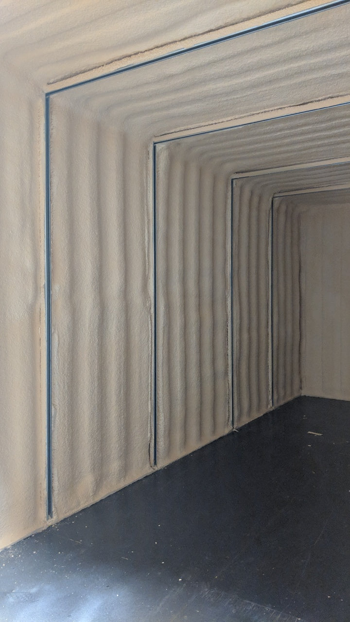 Interior of a shipping container with spray foam insulation and vertical steel strut channels installed for framing or mounting systems.